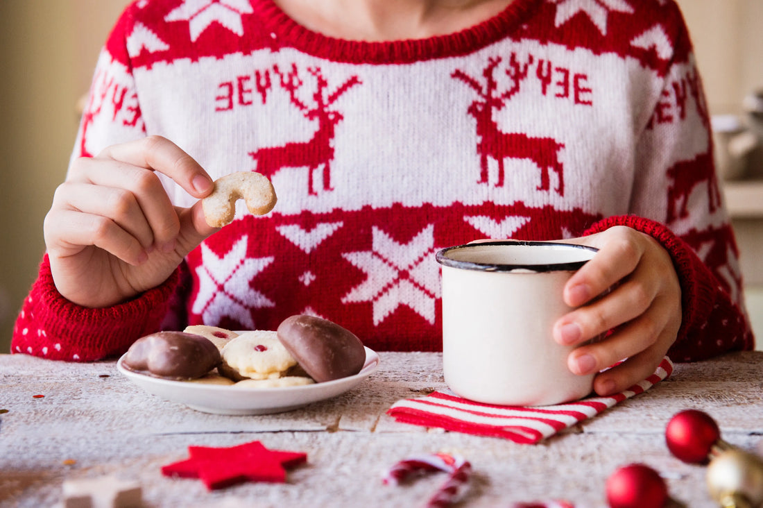 Woman eating Christmas cookies while wearing Christmas sweater. 