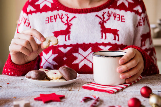 Woman eating Christmas cookies while wearing Christmas sweater. 